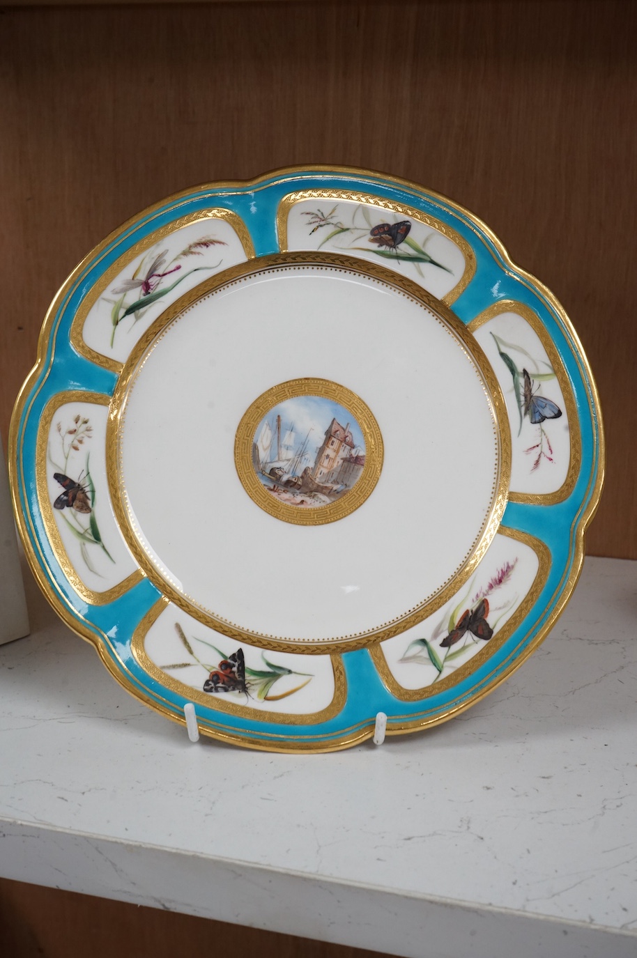 A Minton turquoise and gilt cabinet plate, decorated with butterflies and central continental harbour scene, 24cm diameter.
